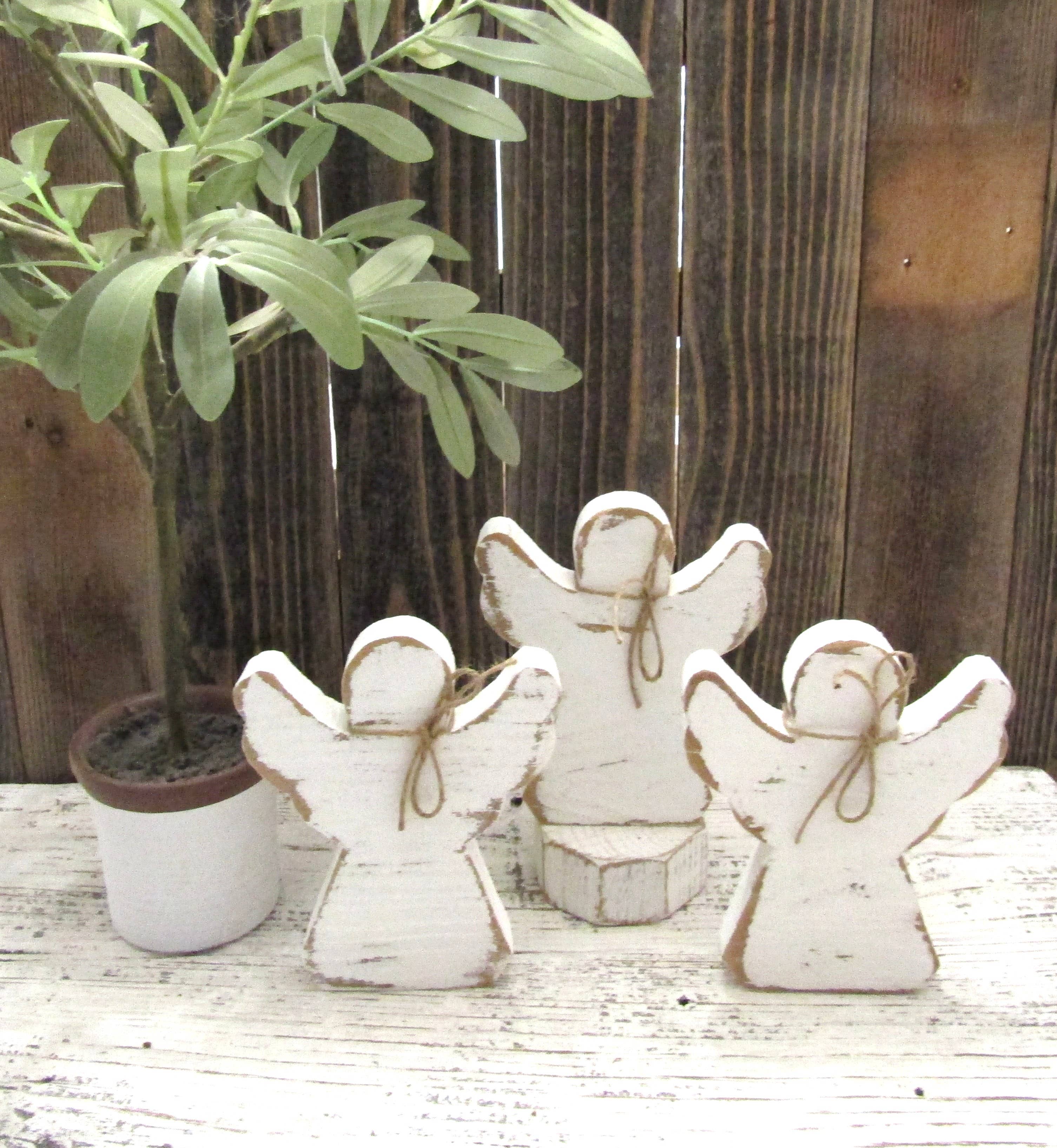 Three distressed white wood angels in assorted sizes with jute bows on a farmhouse shelf