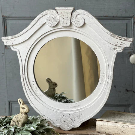 Decorative white round mirror with intricate details on a rustic surface.