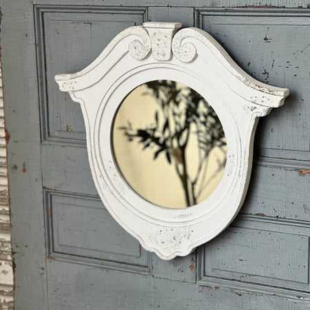 Decorative white mirror with intricate frame on a gray wooden wall