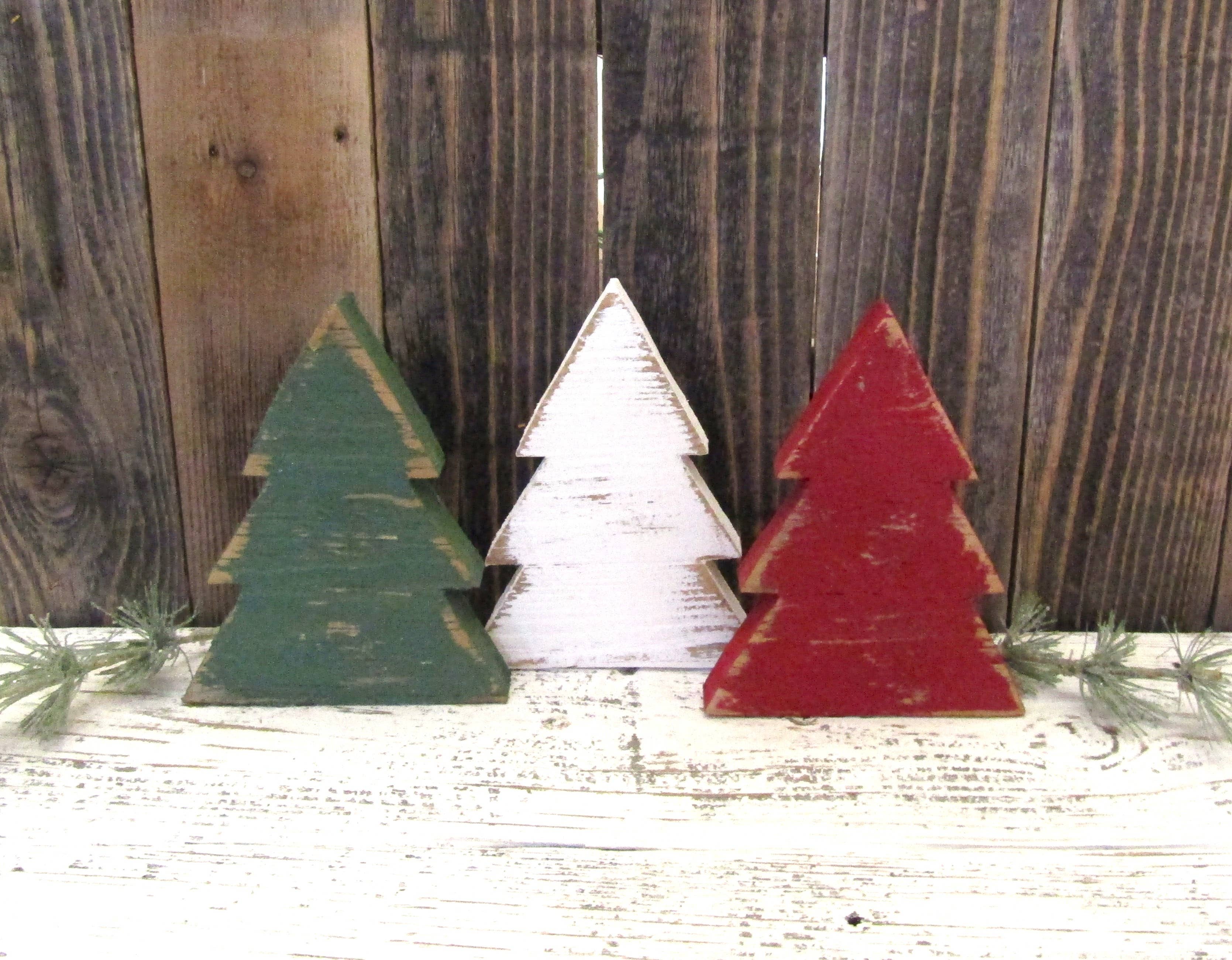 Green, white and red rustic wood Christmas trees standing together with pine sprigs