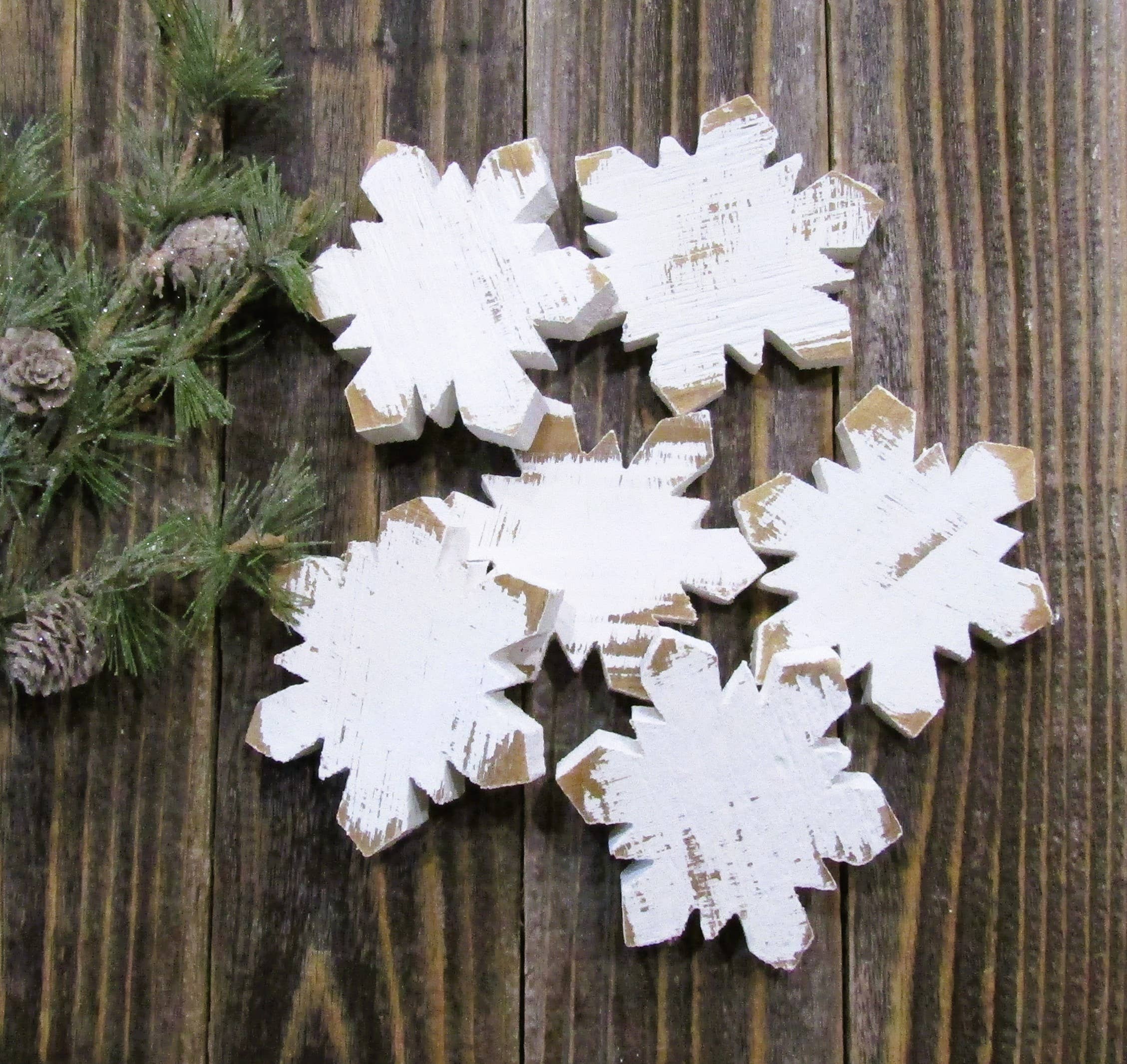 Six white distressed wood snowflakes scattered on dark barn wood with pine sprigs and pinecones