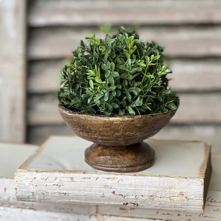 Green artificial topiary in a wooden bowl on a white surface with a wooden background