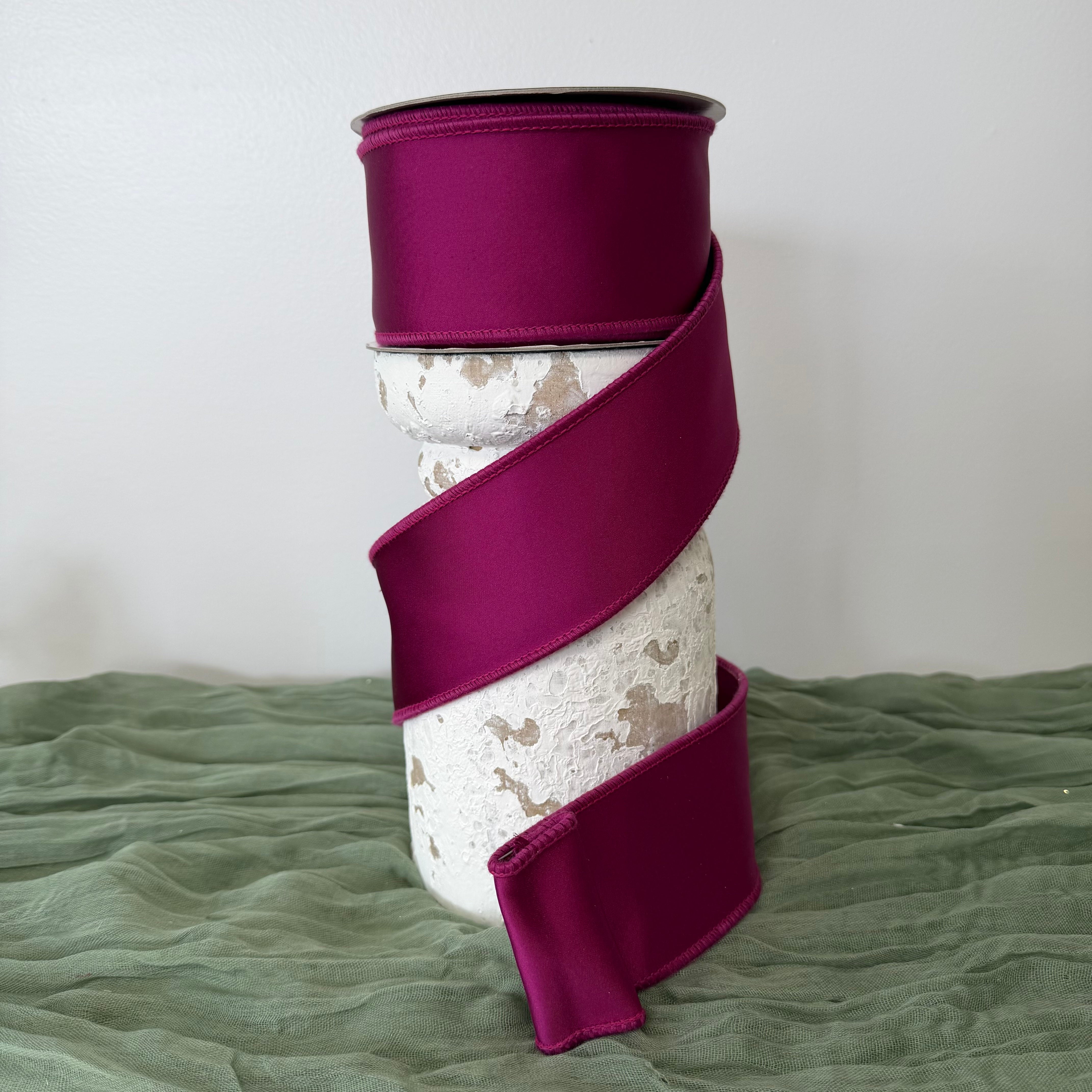 Roll of luxury 2.5 inch purple satin wired ribbon with double fused edges by John Mark Enterprises displayed on a decorative pedestal.