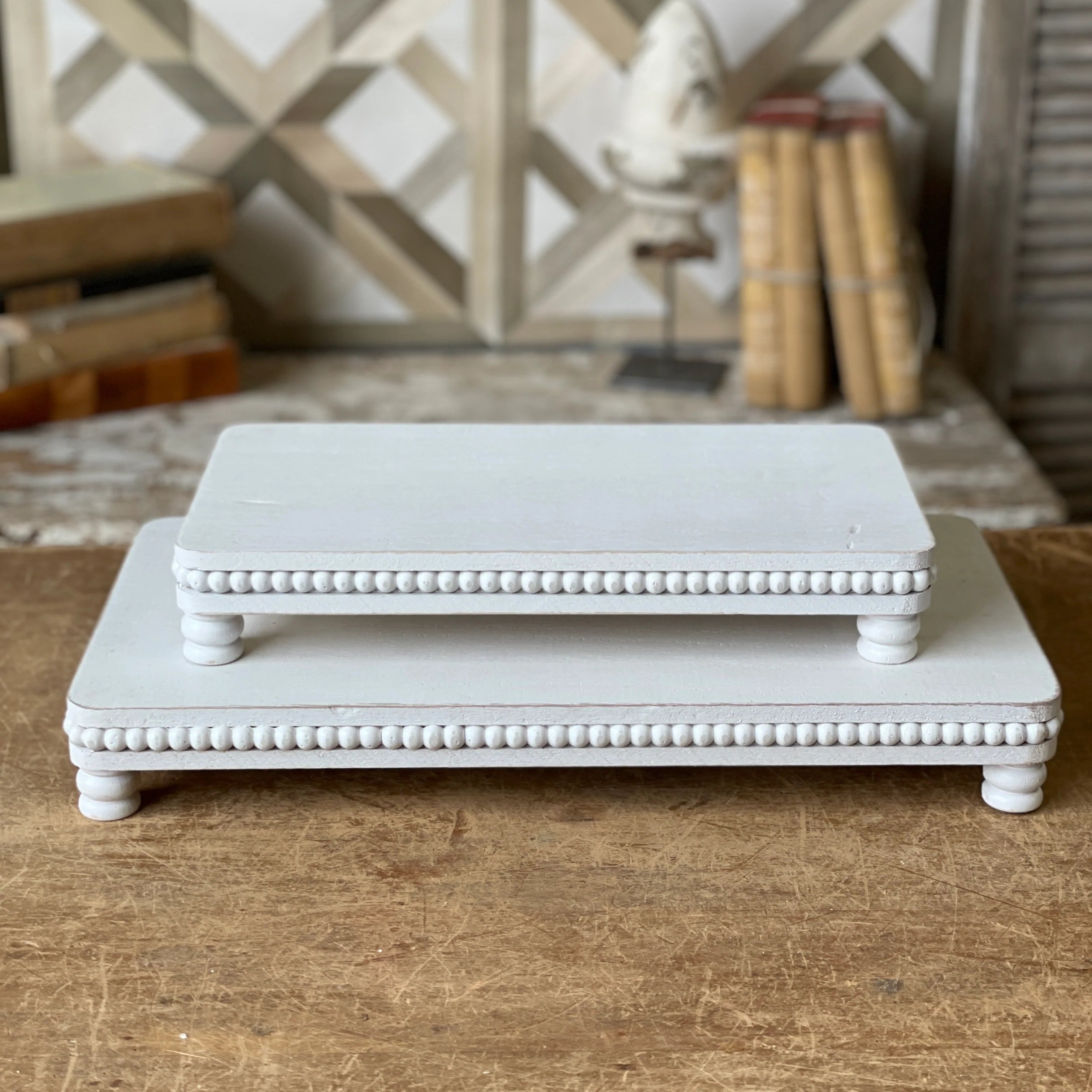 Two white decorative stands on a wooden surface with a geometric wall pattern in the background.