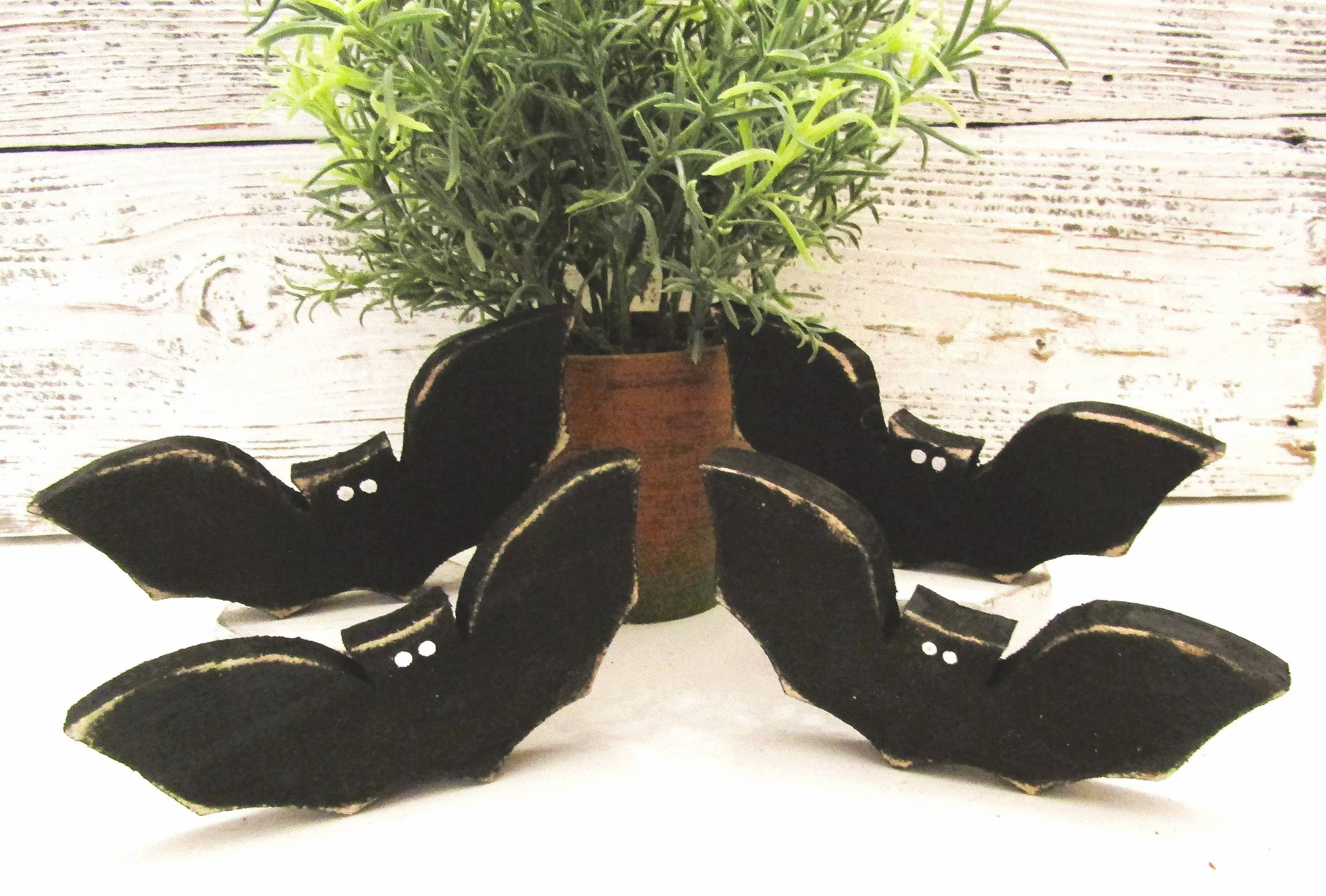 Small black wood Halloween bats with white eyes arranged around a potted plant