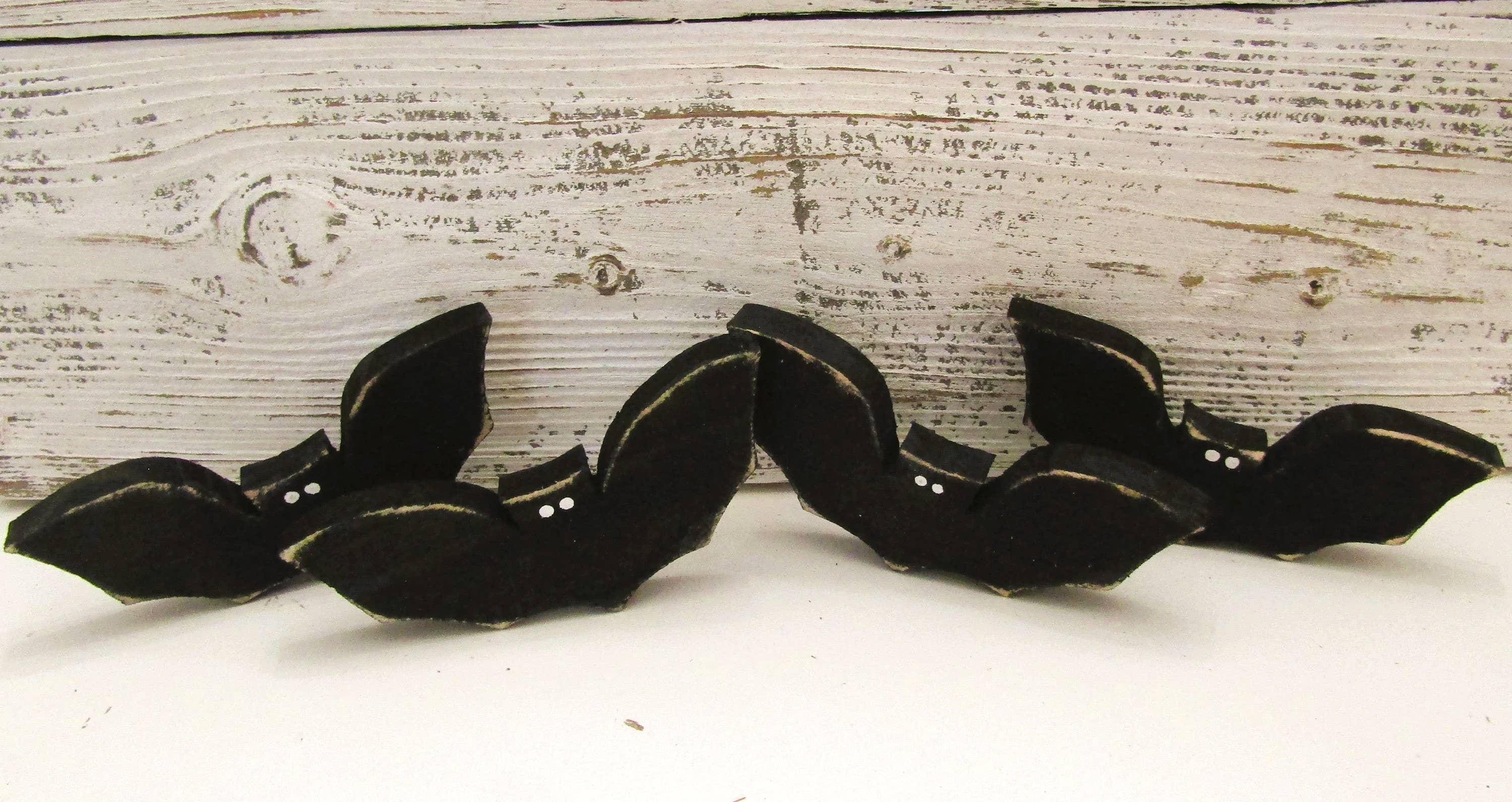 Row of small black wood bats standing on their own on a white distressed wood surface