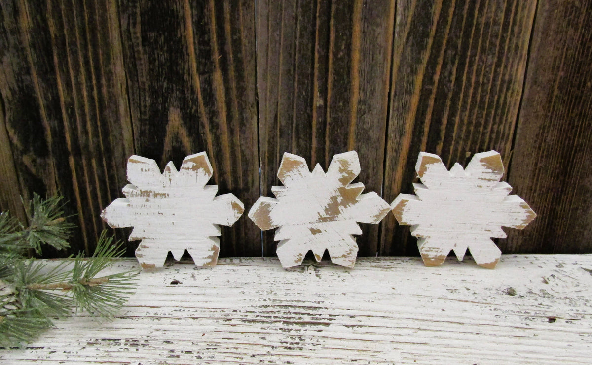 Three small white wood snowflakes standing in a row against weathered barn wood