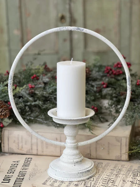 Decorative white metal ring candle holder with a white candle on a rustic background.