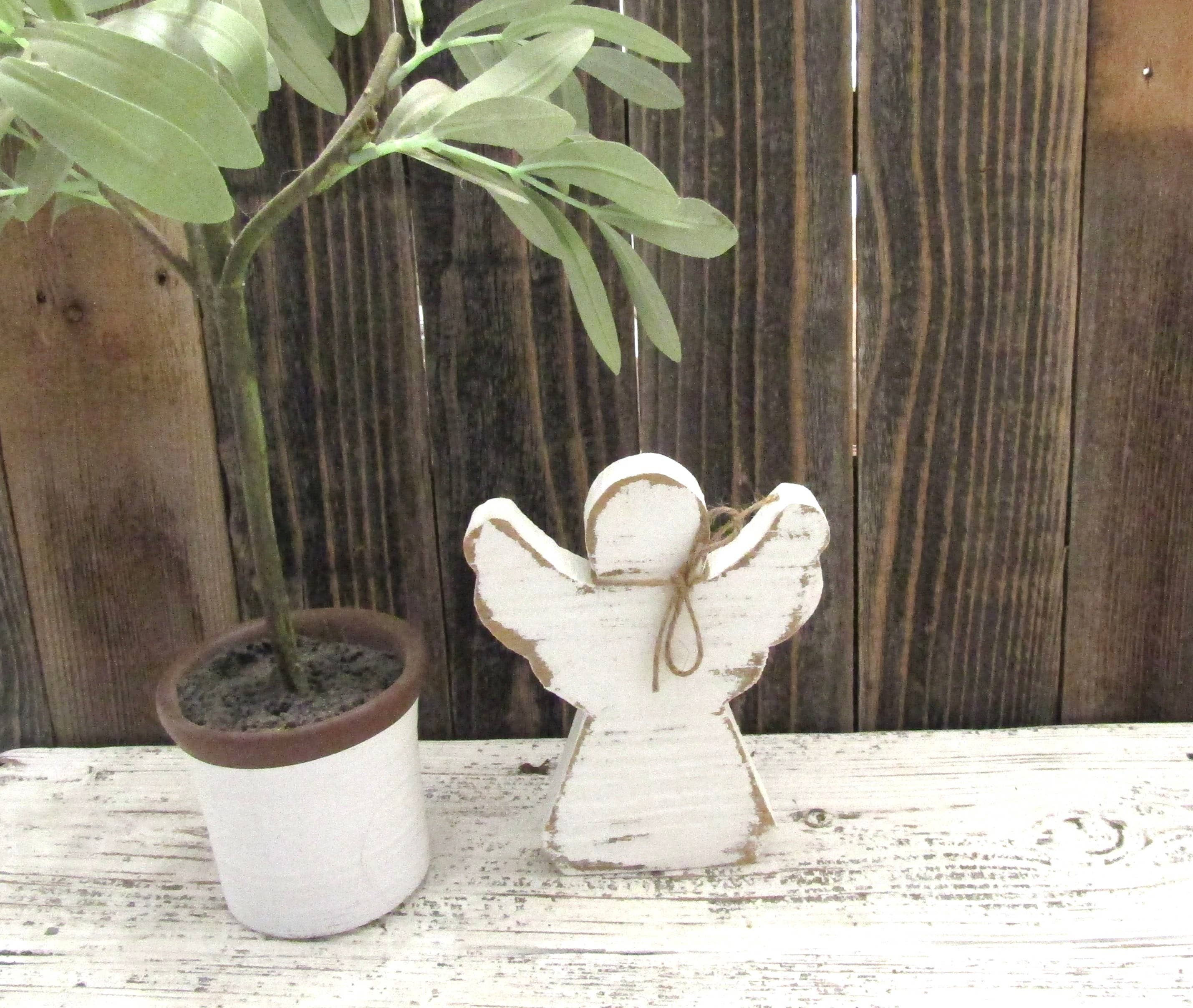Rustic wood angel with jute bow standing on white barn wood beside a potted plant