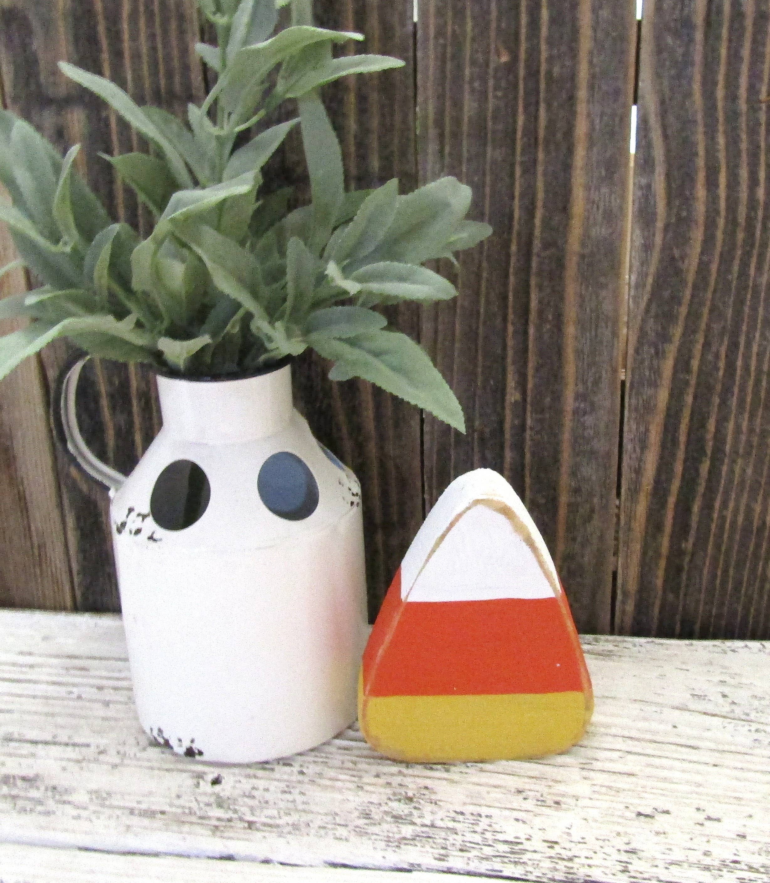 Single rustic wood candy corn standing next to a white pitcher against barn wood