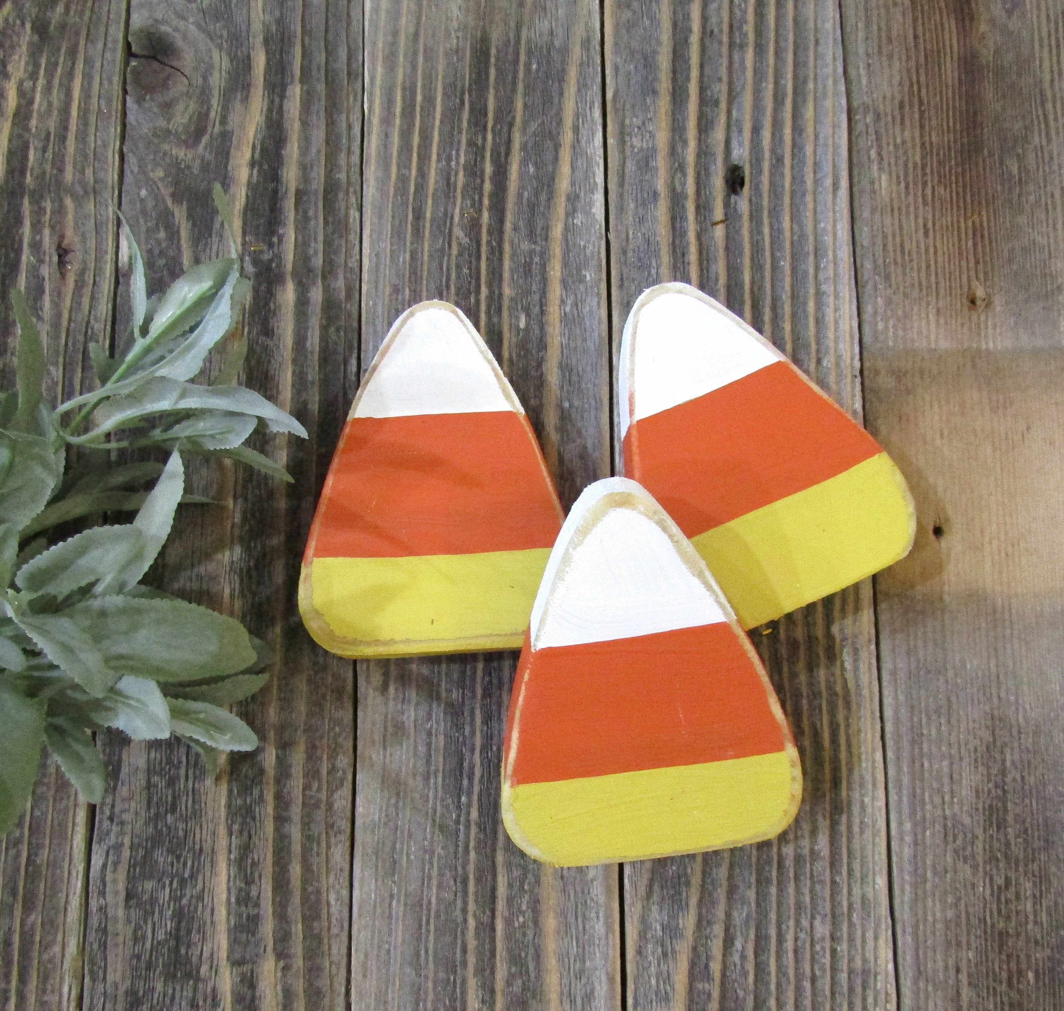 Close up of three distressed wood candy corn pieces showing white, orange and yellow stripes