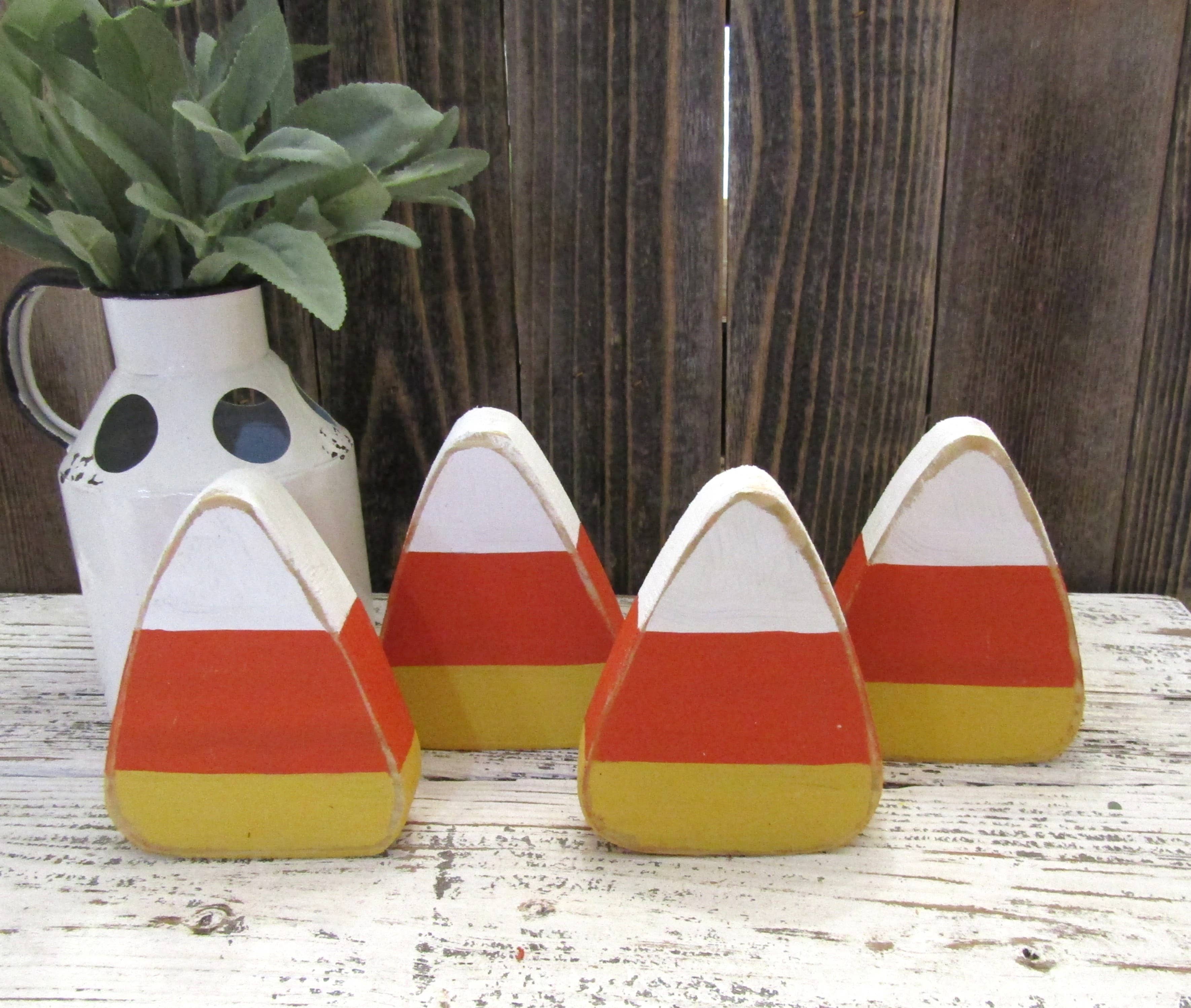 Four hand painted wood candy corn pieces in assorted sizes standing on a wood shelf