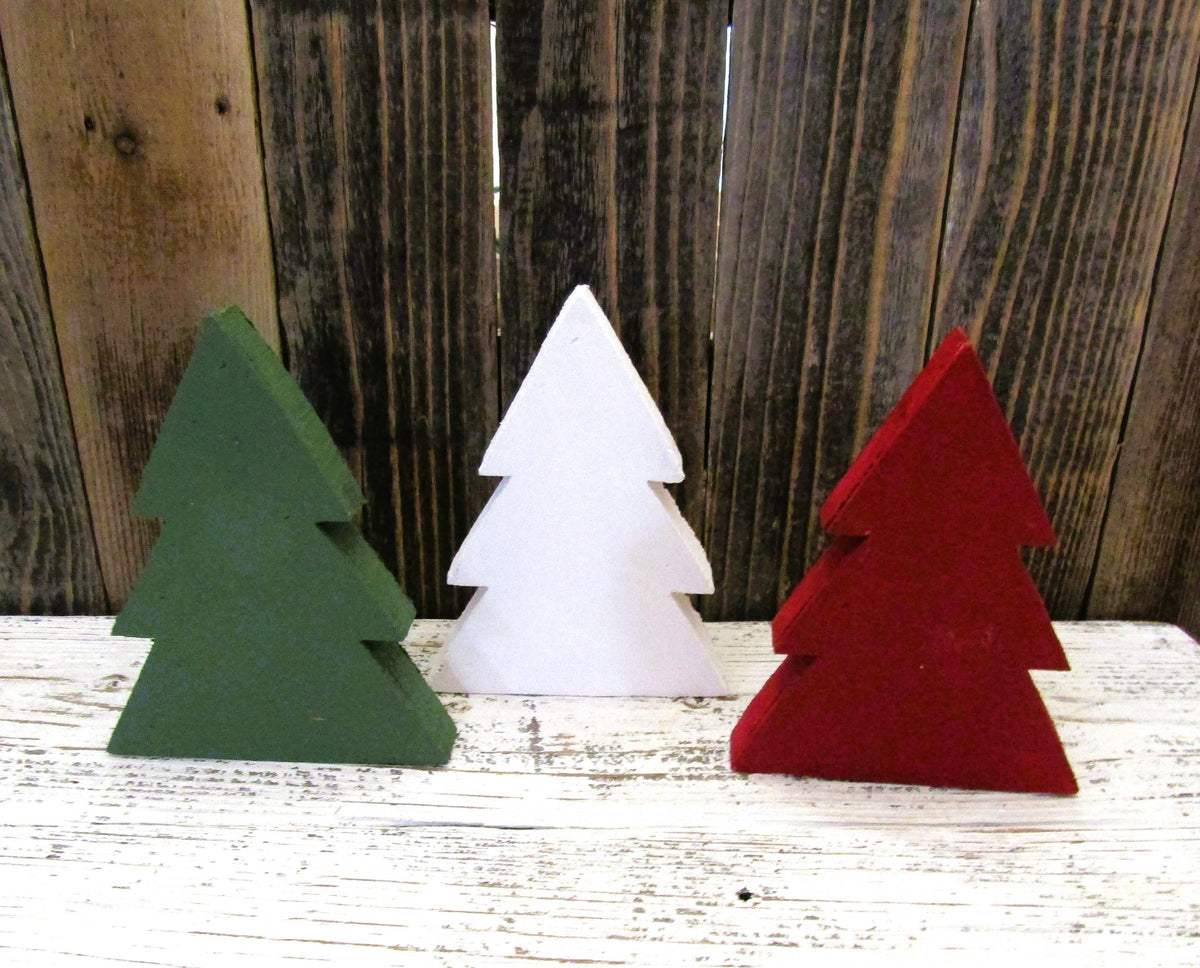 Three 5 3/4 inch rustic wood Christmas trees in green, white and red lined up on a shelf