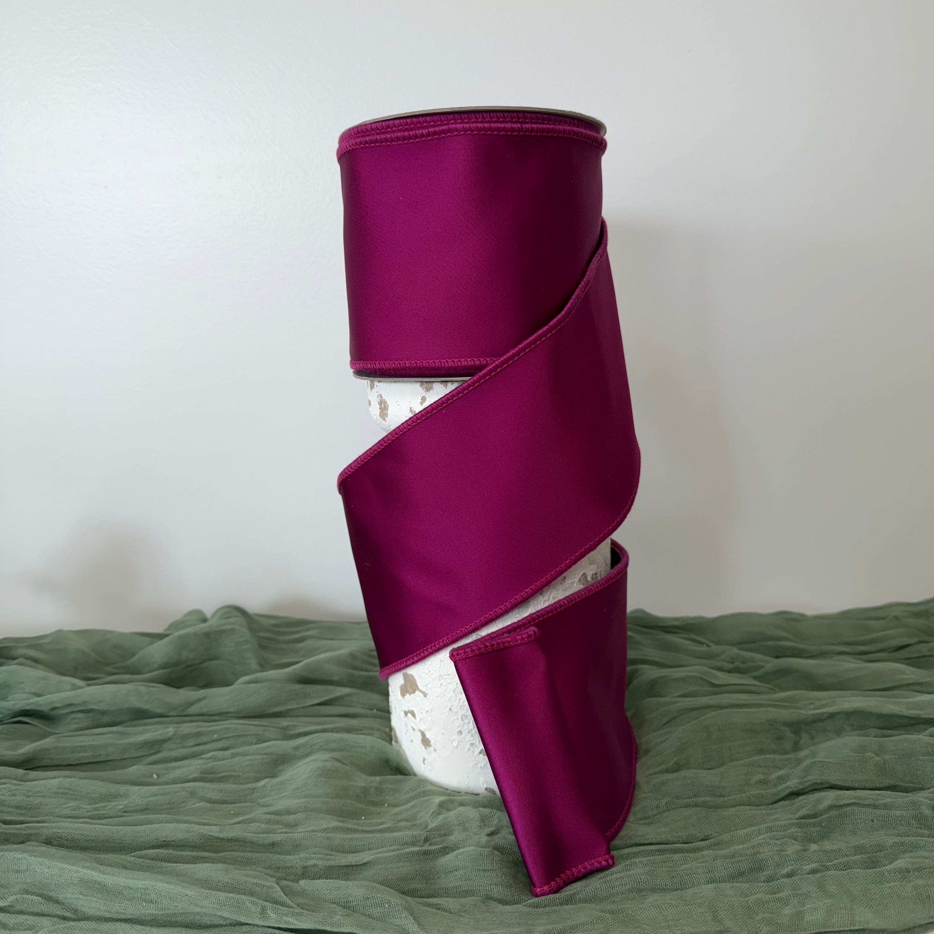 Roll of luxury 4 inch purple satin wired ribbon with double fused edges by John Mark Enterprises displayed on a decorative pedestal.