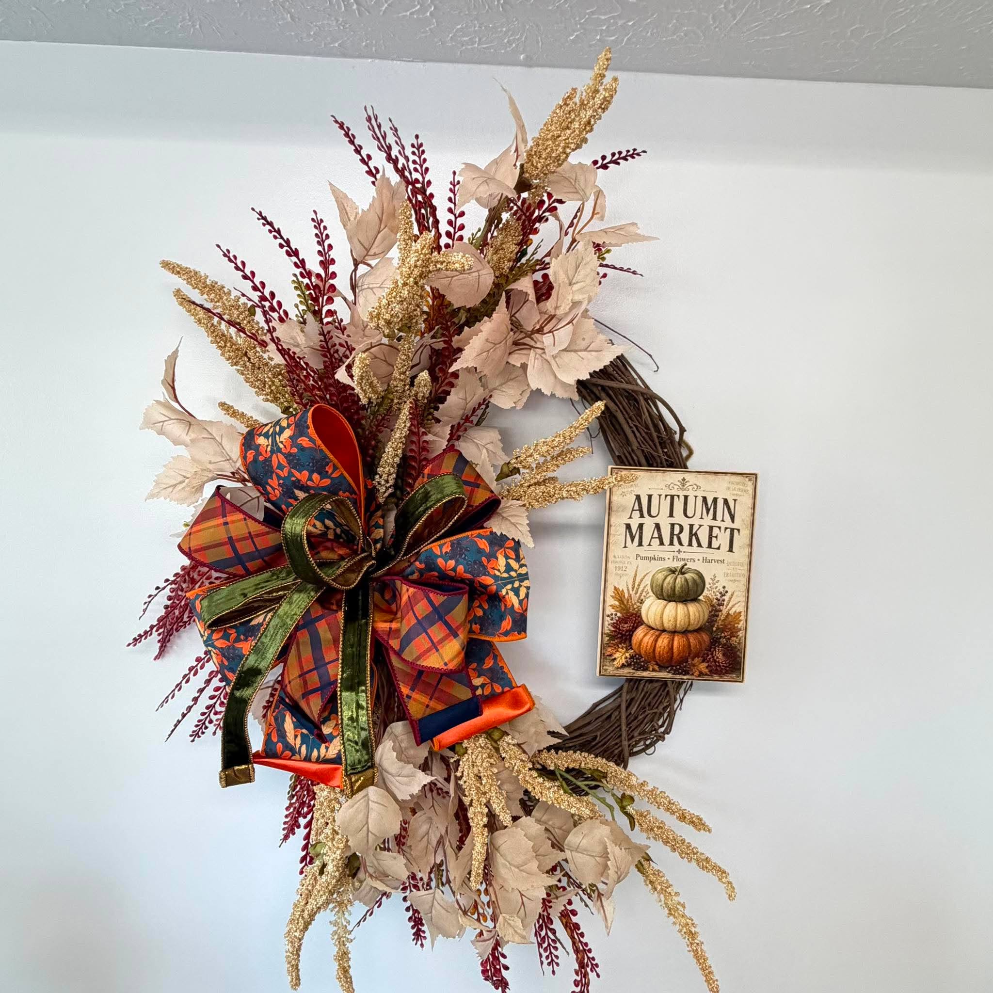 Crescent design of the Autumn Market wreath with florals on one side and bare grapevine holding the sign