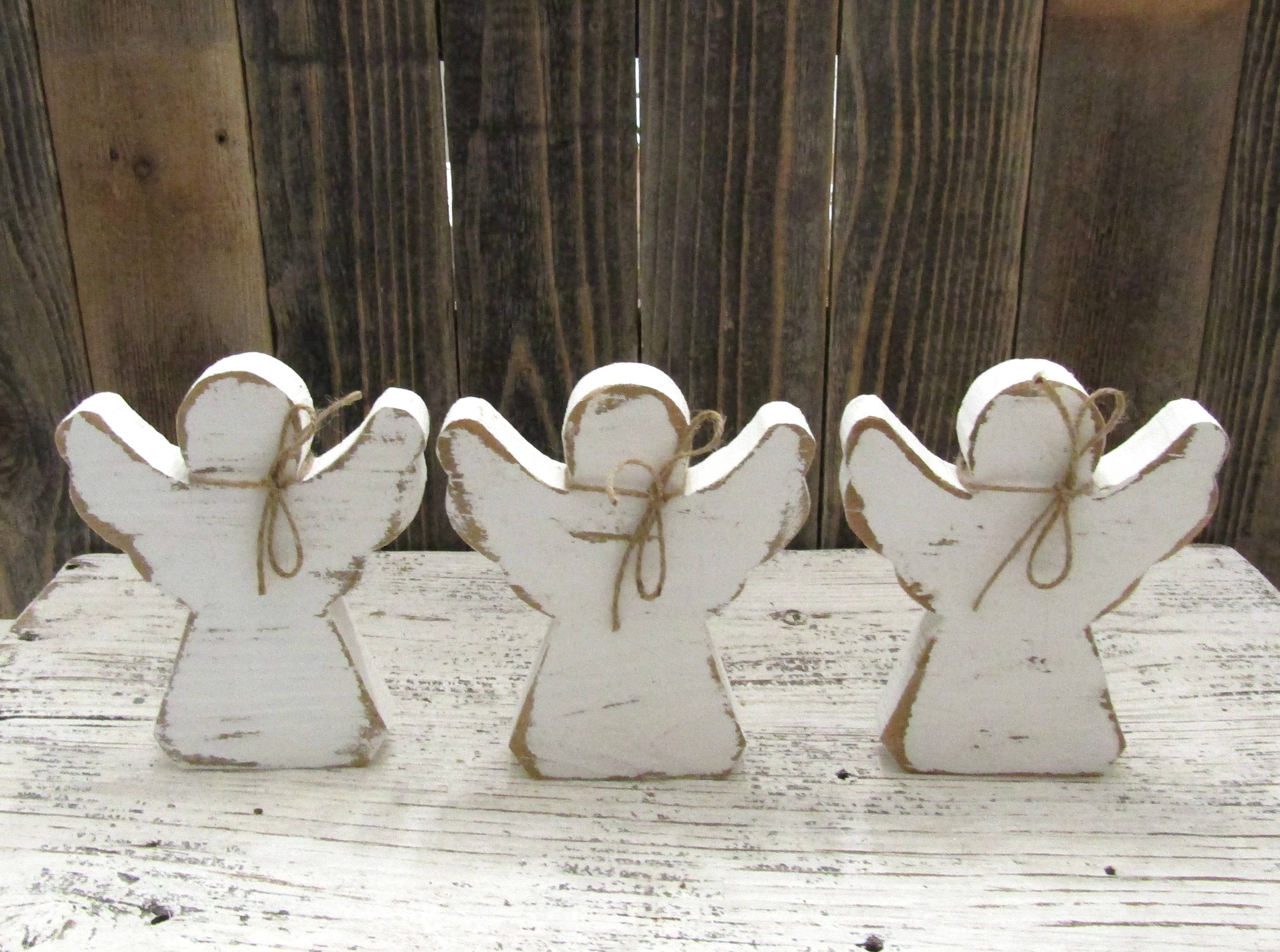 Three 6 inch rustic wood angels with jute bows lined up against weathered barn wood