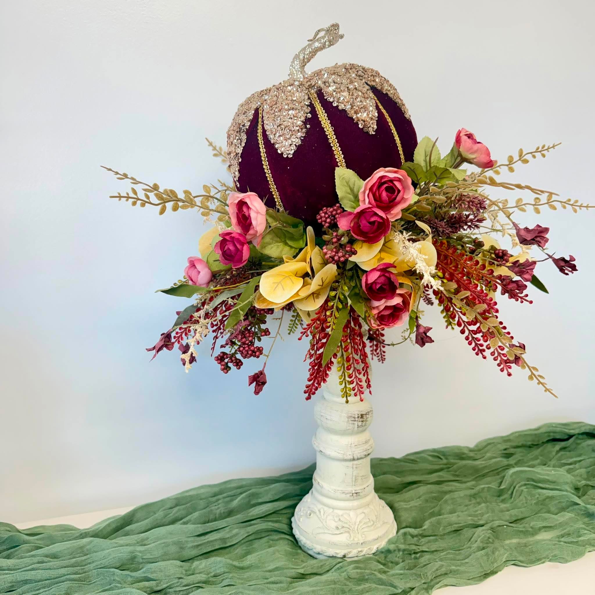 Handmade fall centerpiece with a burgundy velvet sequin pumpkin above a collar of roses and berries