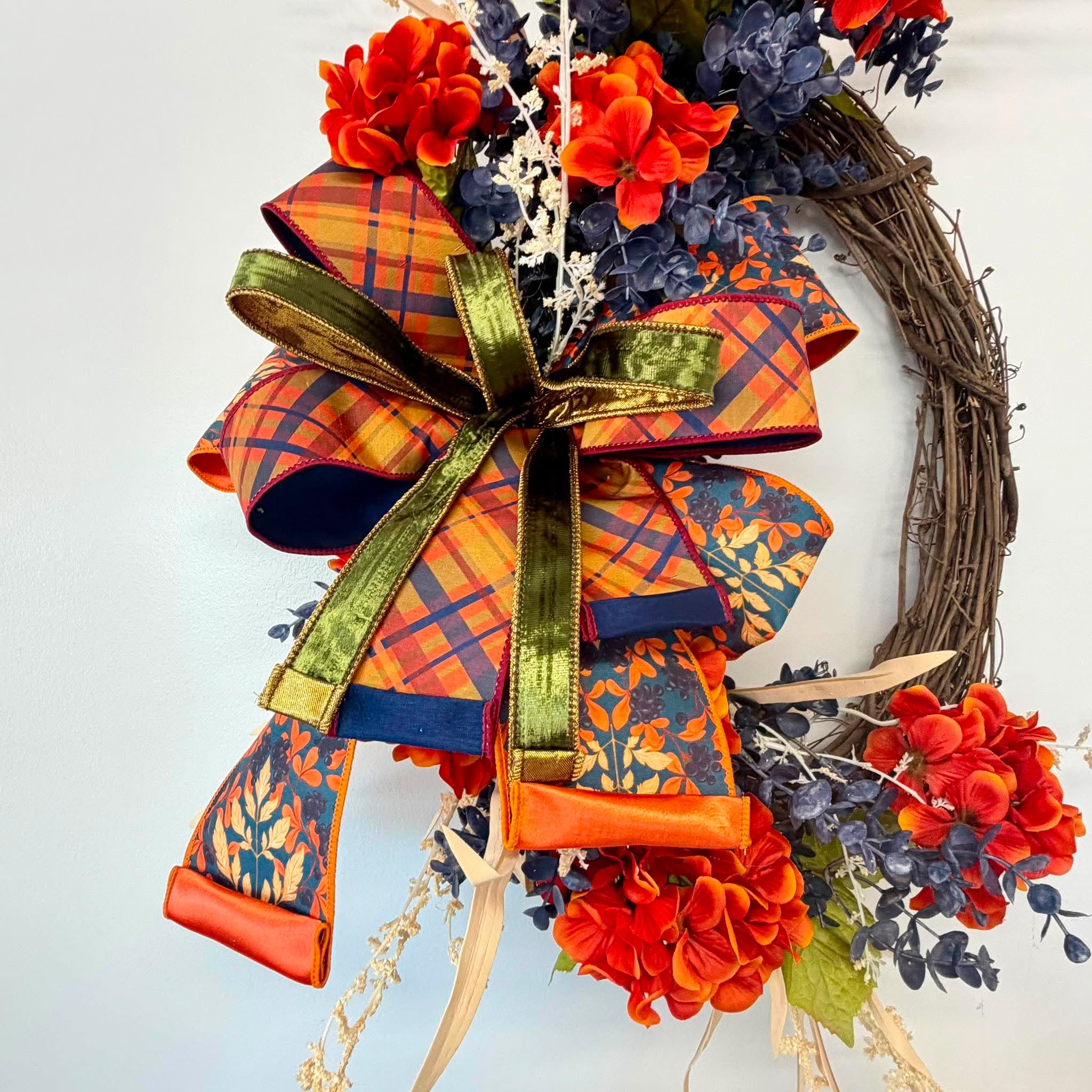 Orange and navy fall wreath with plaid, teal and green velvet ribbon bow and raffia blades