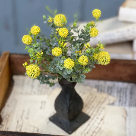 Small bouquet of yellow flowers in a dark vase on an old newspaper